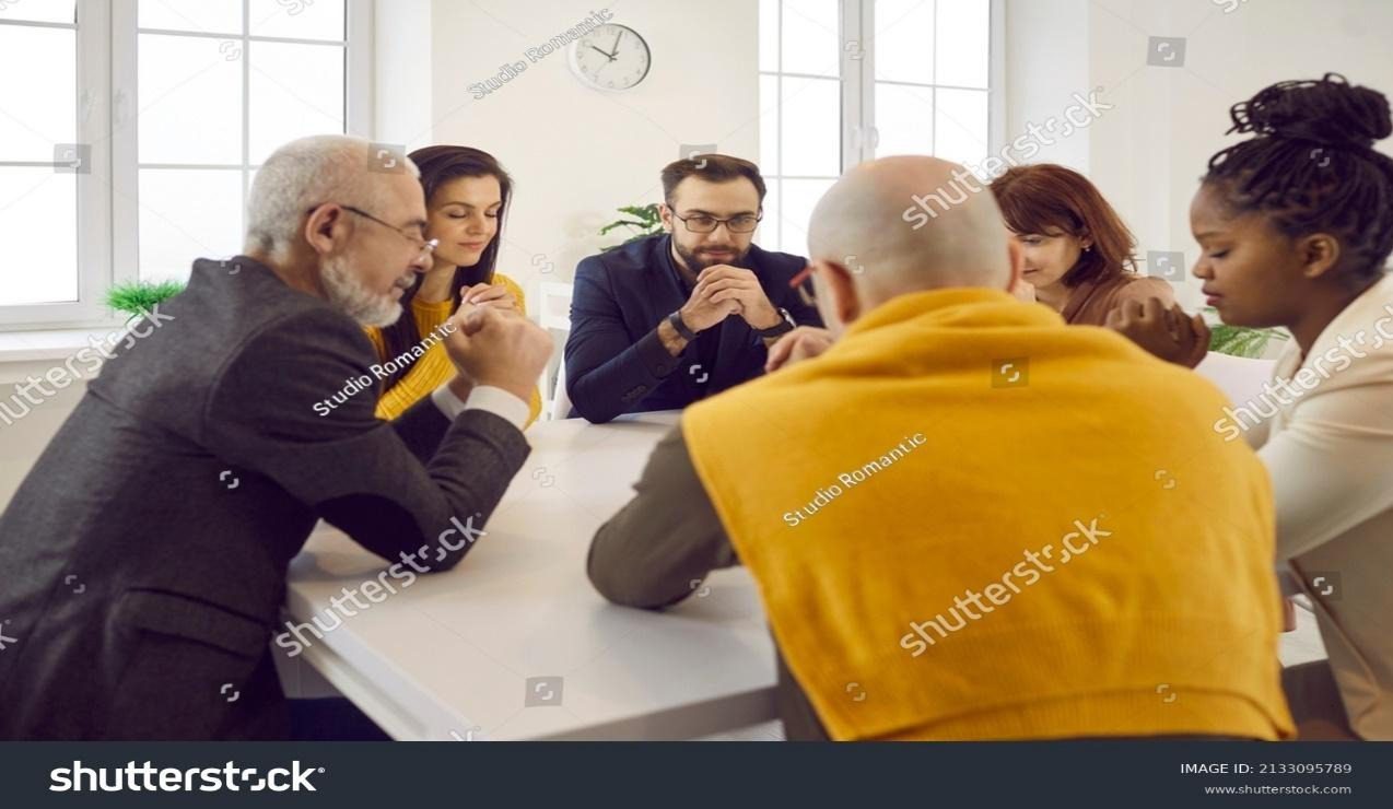 Diverse people praying together. Group of different religious multiracial multiethnic males and females sitting around table and saying prayer of gratitude, thanking God for His amazing grace Sinful